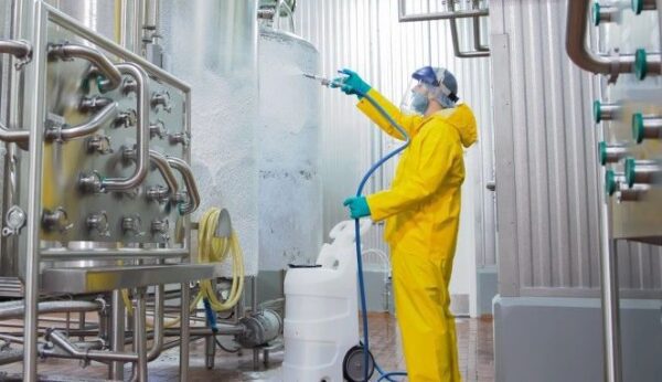 A man in yellow suit spraying water on the floor.