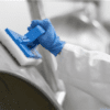 Person wearing gloves cleans a metal surface.