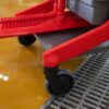 Red cleaning cart with brush and wheels.